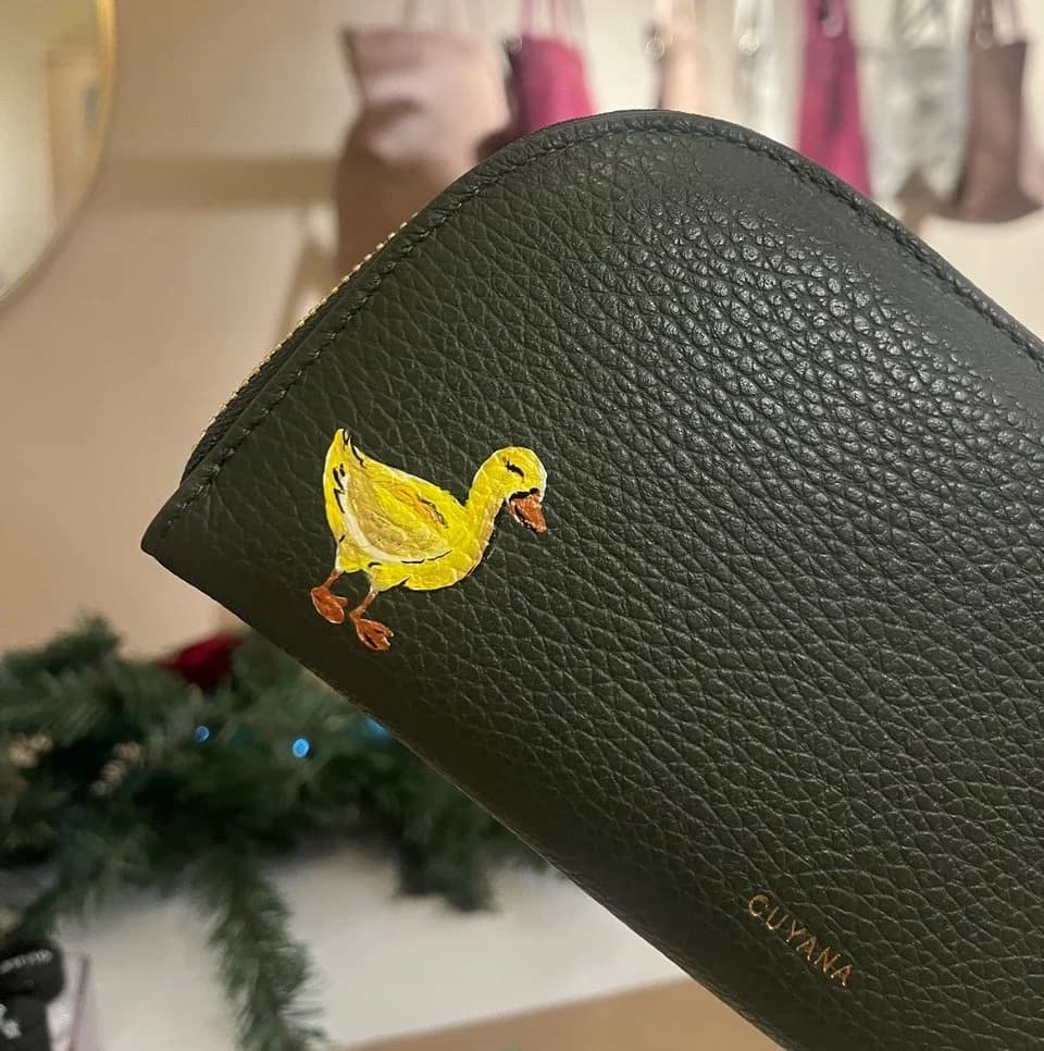 A small yellow duckling painted onto a dark green leather wallet.