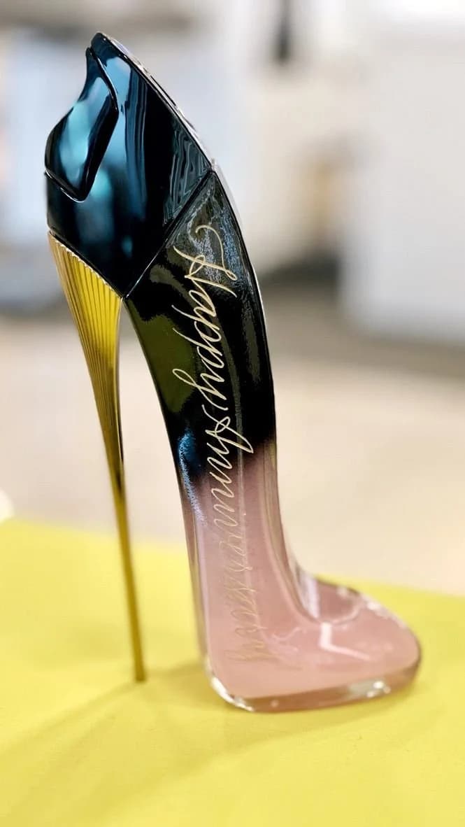 A heel-shaped fragrance bottle personalized with gold script lettering, on a yellow surface.